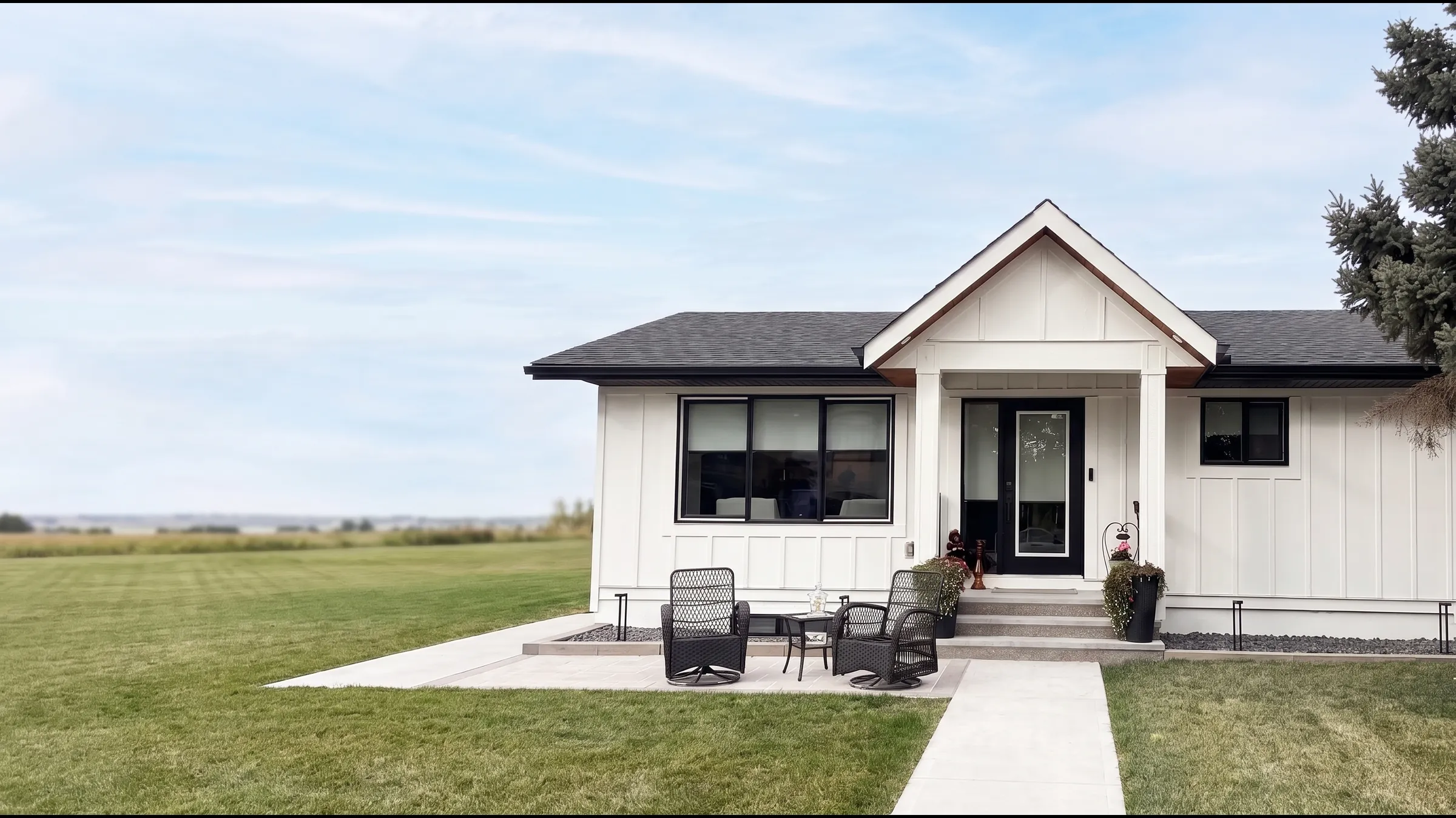 A white board-and-batten bungalow with black windows and door, repainted from grey to white