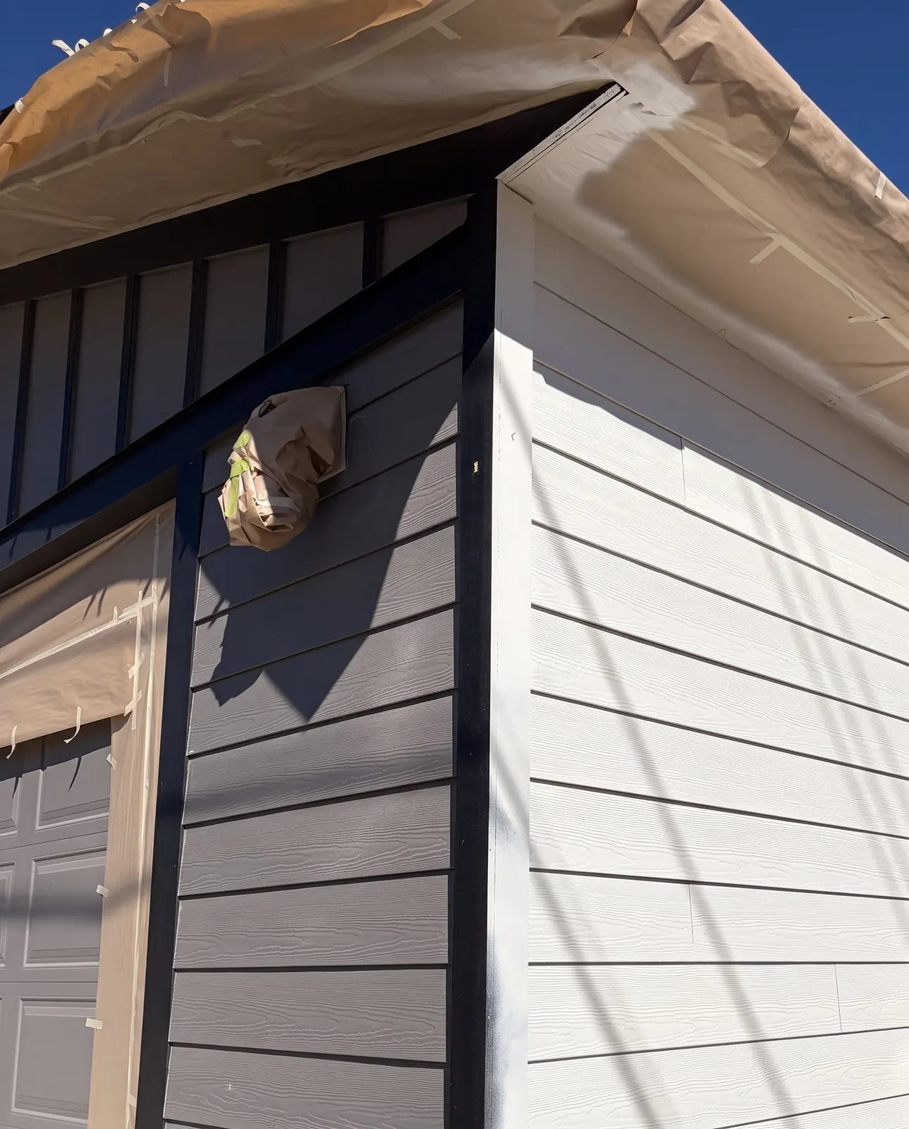 Fresh white siding meeting dark grey board-and-batten, eaves still papered